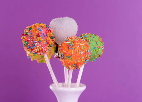 Söta cake pops i vas på lila bakgrund — Stockfoto