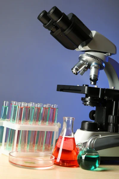 Microscopio e provette su tavola, su sfondo a colori — Foto Stock