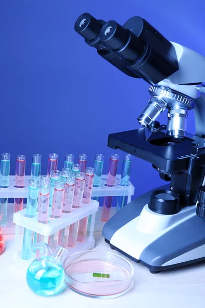 Microscoop en reageerbuizen op tafel, op kleur achtergrond — Stockfoto