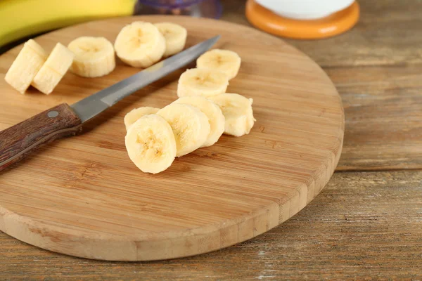 Banane tranchée sur planche à découper, sur fond bois — Photo