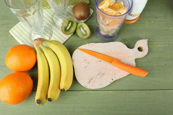 Sliced fruits and blender on wooden table, on wooden background — Stock Photo, Image