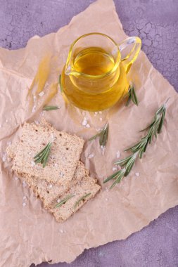 Crispbread tuz, yağ sürahi ve dal biberiye buruşuk kağıt ve renkli ahşap arka plan parçası üzerinde