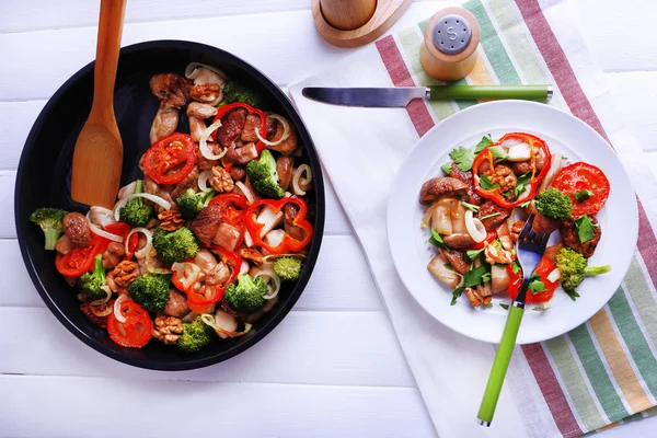Тушковані дикі гриби з овочами та спеціями на сковороді та тарілкою на столі — стокове фото