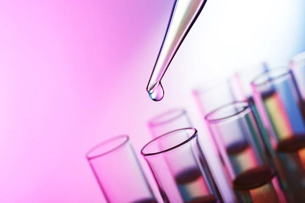 Pipette adding liquid to the one of test-tubes on the pink shining background — Stock Photo, Image