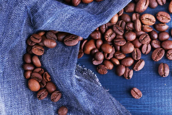 Verschüttete Kaffeebohnen auf blauem Holzhintergrund mit Jeansmaterial — Stockfoto