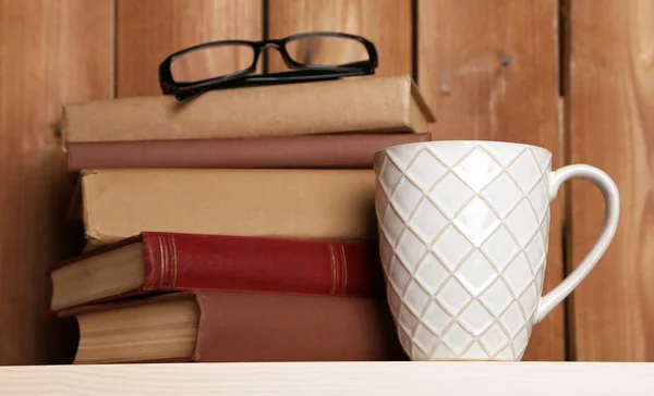 Stapel boeken met cup en bril op tafelblad en houten achtergrond — Stockfoto