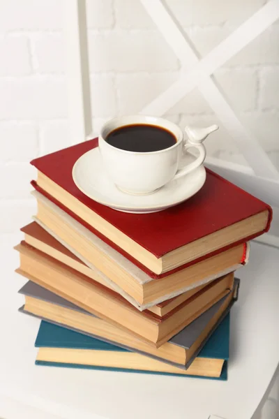 Hromadu knih s šálkem horkého nápoje na židli na cihlovou zeď na pozadí — Stock fotografie