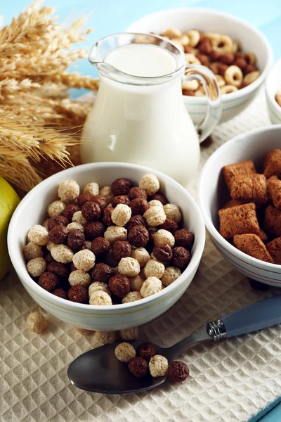 Verschillende sweet granen in keramische kommen, fruit en kruik met melk op servet, op een houten achtergrond kleur — Stockfoto