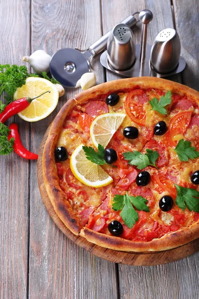 Tasty pizza with spices and round knife on board and wooden table background — Stock Photo, Image