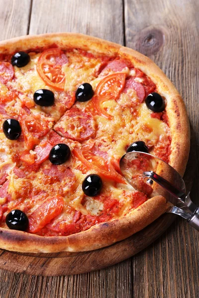 Gustosa pizza con olive nere e coltello rotondo a bordo e sfondo tavolo in legno — Foto Stock
