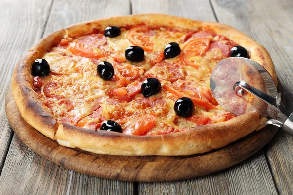 Ízletes pizza fekete olajbogyó és a kerek kést, és fából készült asztal háttere — Stock Fotó