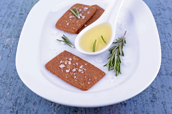 Crispbread with salt, spoon of oil and sprigs of rosemary on plate, on color wooden table background — Stock Photo, Image