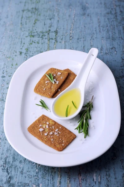 Crispbread with salt, spoon of oil and sprigs of rosemary on plate, on color wooden table background — Stock Photo, Image