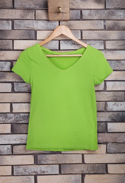 Vrouwelijke t-shirt op hanger op bakstenen muur achtergrond — Stockfoto