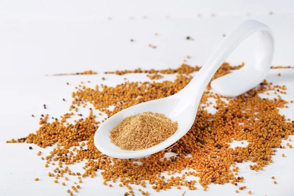 Mustard powder in spoon on mustard seeds, on  wooden background — Stock Photo, Image