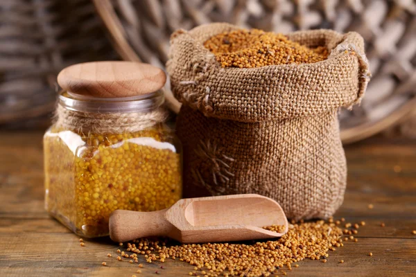 Mustard seeds in bag and Dijon mustard in glass jar on wooden background — Stock Photo, Image