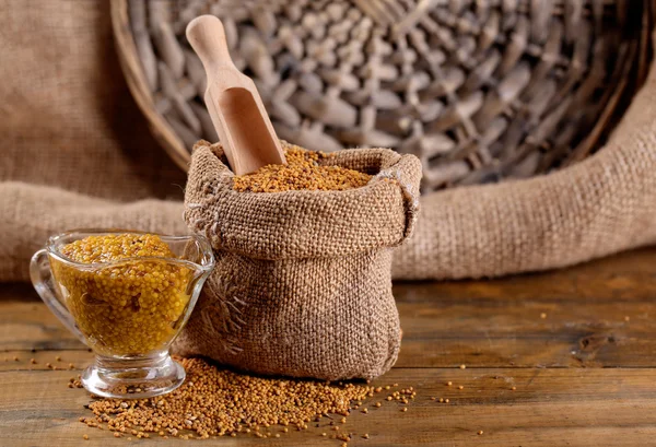 Graines de moutarde en sac et sauce en saucière sur fond bois — Photo