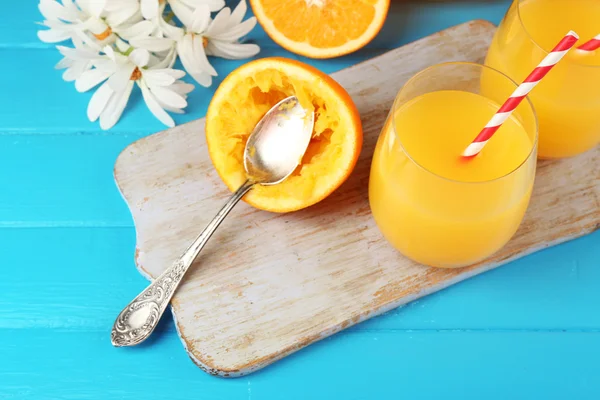 Glass of orange juice with slices, flowers and straws on cutting board on color wooden background — Stock Photo, Image