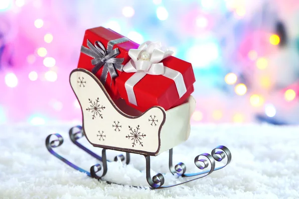 Sledge de brinquedo de madeira com presentes de Natal no fundo brilhante — Fotografia de Stock
