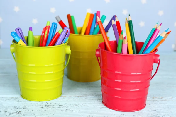 Trois tasses en plastique avec différents stylos, crayons et marqueurs sur table en bois de couleur sur table en bois de couleur et fond bleu avec des étoiles imprimées — Photo