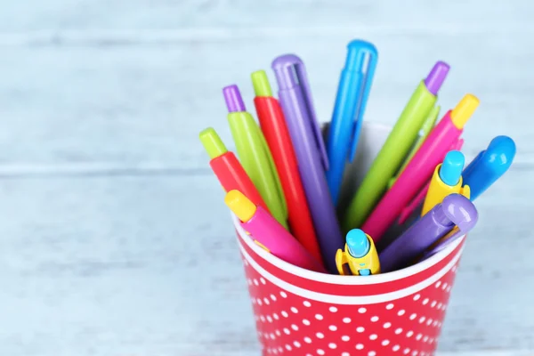 Copa de plástico con diferentes plumas en el fondo de madera de color — Foto de Stock