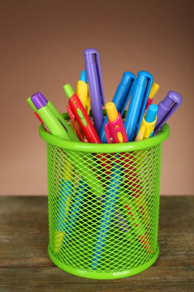 Bolígrafos coloridos en soporte de metal verde en mesa de madera y fondo de color sombreado —  Fotos de Stock