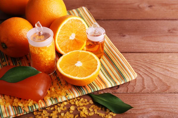 Spa ainda vida com laranjas, garrafas de sal de banho e óleo, e barra de sabão em guardanapo listrado em fundo de madeira — Fotografia de Stock