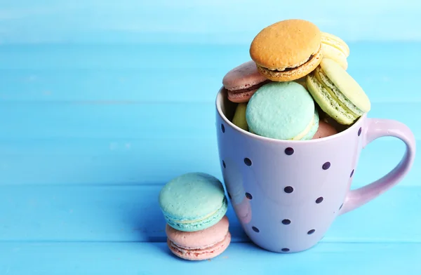 Assortment of gentle colorful macaroons in colorful mug on color wooden background — Stock Photo, Image