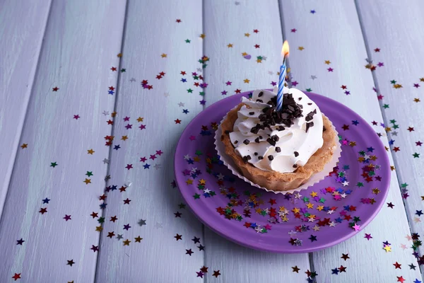 Pastel de la taza del cumpleaños con vela y destellos en el plato en color fondo de madera — Foto de Stock