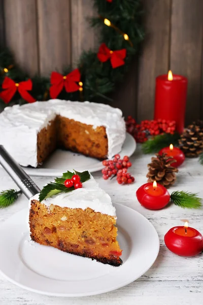 Кусок торта, покрытый сливками с рождественским декором на столе, на фоне деревянной стены — стоковое фото