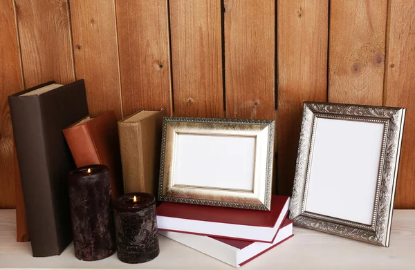 Photo frames with candles and books on wooden surface and wooden wall background — Stock Photo, Image