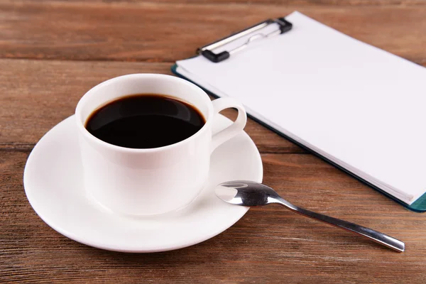 Tasse Kaffee auf Untertasse mit Blatt Papier und Stift auf Holztischhintergrund — Stockfoto