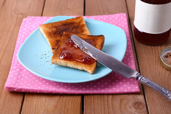 Plaka ve peçete reçel kavanoz ahşap masa arka plan üzerinde yakınındaki bıçakla yayılmış tost ekmeği — Stok fotoğraf