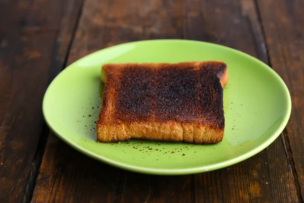 Burnt toast bread on light green plate, on wooden table background — Stock Photo, Image