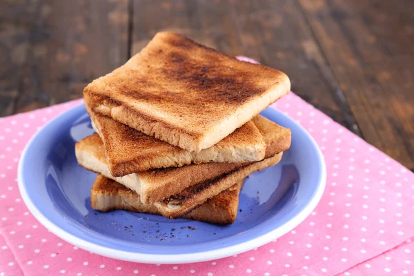 Ahşap masa arka plan üzerinde pembe peçete ile mavi plaka üzerinde tost ekmeği — Stok fotoğraf
