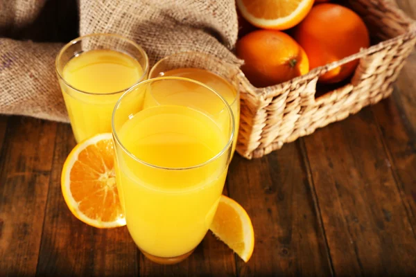杯橙汁与切片和柳条篮子用麻袋布木桌背景 — 图库照片