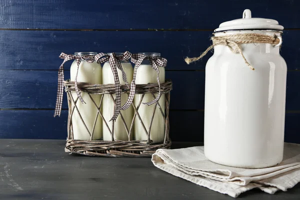 Milk can and glass bottles on color wooden background — Stock Photo, Image