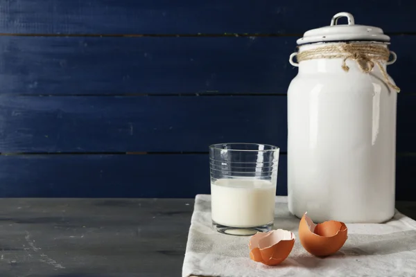 Mjölk kan med glas och äggskal på färg trä bakgrund — Stockfoto