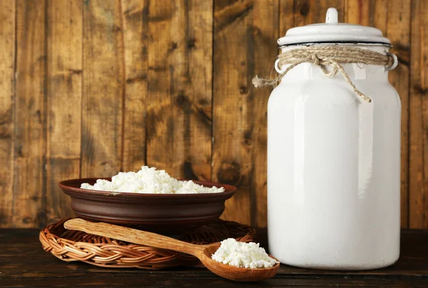 Milk can with bowl of cottage cheese and spoon on rustic wooden background — Stock Photo, Image