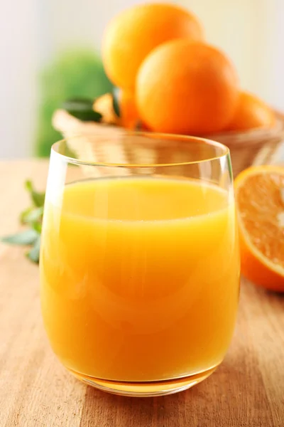 Glass of orange juice and wicker basket with oranges on wooden table background — Stock Photo, Image