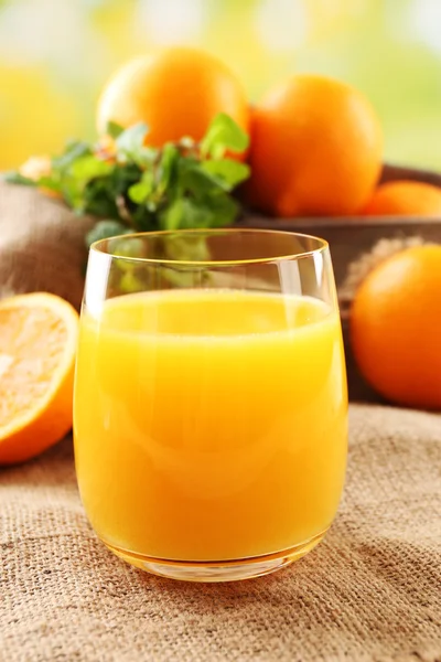 Glass of orange juice on wooden table with burlap cloth and bright background — Stock Photo, Image