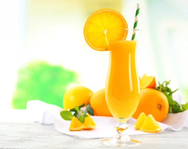 Vaso de zumo de naranja con paja y rodajas sobre mesa de madera y fondo brillante — Foto de Stock