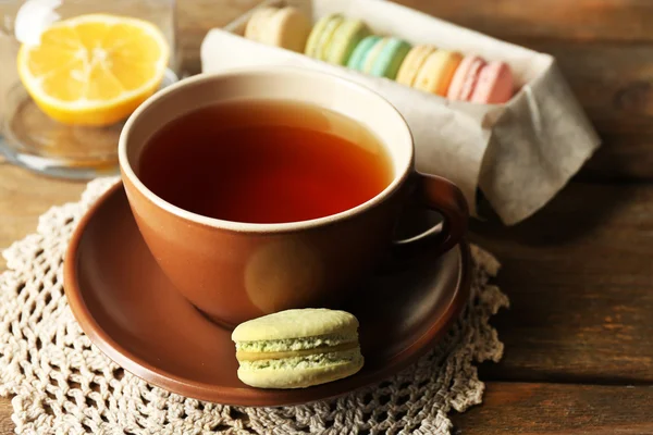 Kleurrijke bitterkoekjes met kopje thee op houten achtergrond — Stockfoto