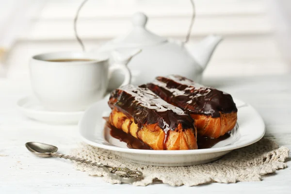 Smakelijke eclairs en kopje thee op houten tafel — Stockfoto