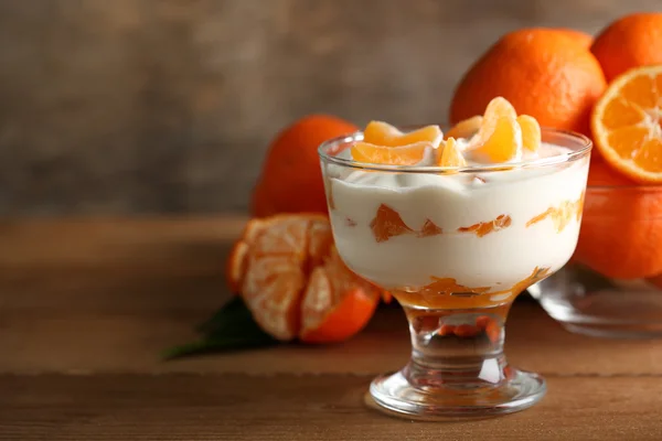 Sabroso postre de leche con trozos de mandarina fresca en tazón de vidrio, sobre fondo de madera — Foto de Stock