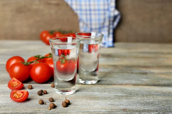 Glasses of ouzo and tomatoes on wooden table — Stock Photo, Image