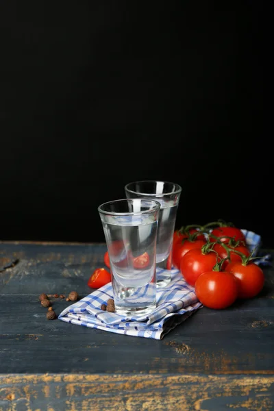 Óculos de ouzo e tomates sobre mesa de madeira, sobre fundo cinzento — Fotografia de Stock