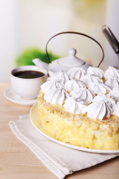 Tasty homemade meringue cake and cup of tea on wooden table, on light background — Stock Photo, Image