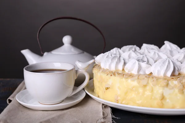 Tasty homemade meringue cake and cup of tea on wooden table, on grey background — Stock Photo, Image