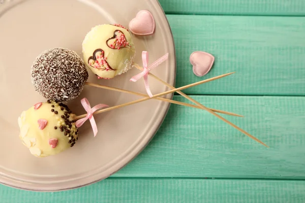 Tasty cake pops on plate, on wooden table — Stock Photo, Image